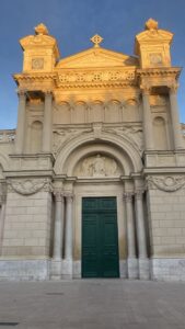 Image of the sun setting on the church from the middle ages, Église de la Madeleine. It has intricate stone work and a dark green door.