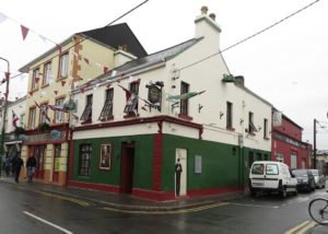 The outside view of the Crane Bar from right outside. A green, red, and white building in the traditional 1800s Irish style. a small figure painted on the outside indicated the live music. 