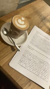 Image of a table with a cappuccino and homework sitting next to it.