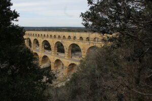 Image of the Roman aqueduct, Pont du Gard. It is framed by trees on both sides with the three tiered aqueduct in the center.