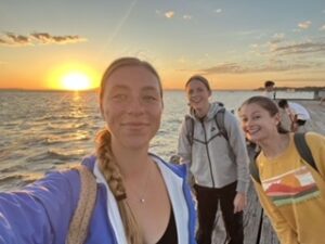 Three girls taking selfie on pier with ocean and sunset behind them