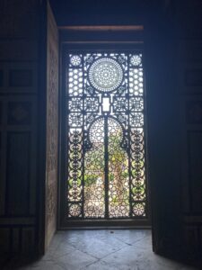 Image of a door in a mosque with the intricate designs in the Islamic art style. Light is shining through the wooden cutouts.