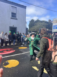 A man clad in green sailor's gear leads the parade.