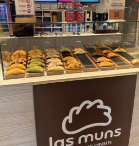 an empanada stand with a colorful tray of different flavors. the sign is a simple empanada design. 