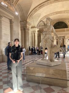 Me standing to the left of a statue in the Greek wing of the Louvre of Artemis.