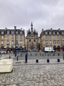 A street in Bordeaux with the bell tower in the center and buildings on wither side.