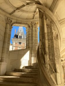 Inside the spiral staircase of Château de Blois with the view from the window framing a brick tower.