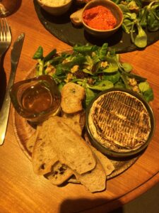 Roasted Camembert on a plate with toasted baguette slices, a salad, and honey.