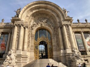 Entrance to le Petit Palais. The doorway is framed with columns and statues, with a staircase leading to the golden doors.