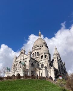 Image of the church, Sacré Coeur, overlooking Paris with clouds and a bright blue sky in the background