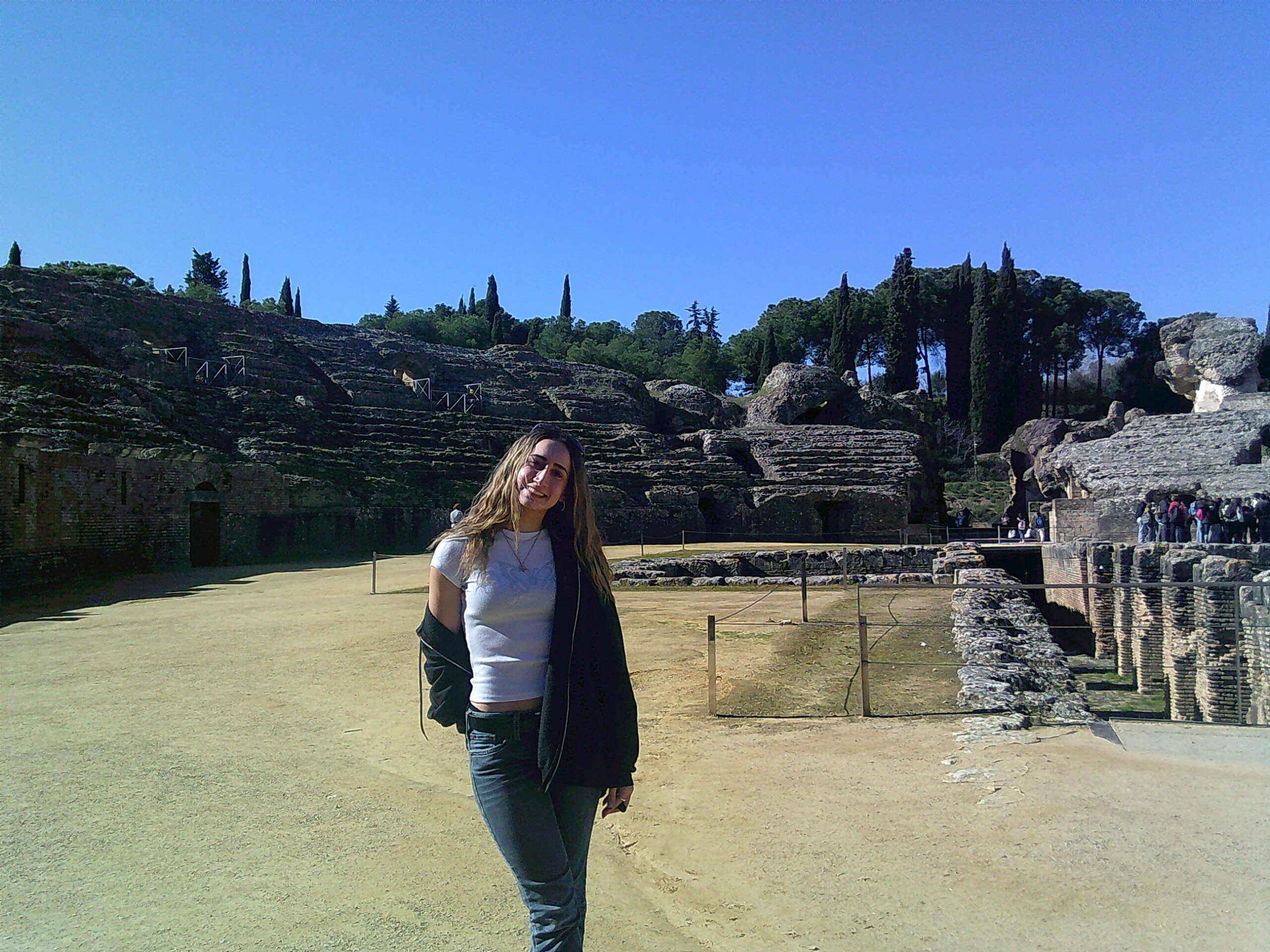 A photo of me at the Itálica roman ruins, with rocky ruins and trees in the background.