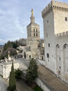 Exterior view of large castle, made of white brick. Blue skies and short trees in the background.