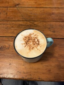 Top view of a blue coffee cup with foam and orange-brown powder sprinkled on top, sitting on top of a wooden table