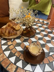 Small cup of espresso with nuts on the rim and two pastries in the background, on a patterned table