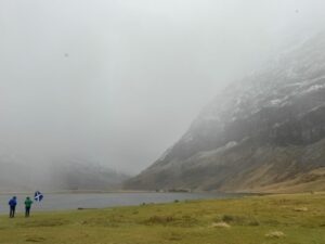 Two people caught in a hail storm. One in neon green raincoat waves Scottish flag