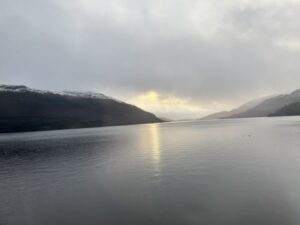 A flat stretch of water, reflecting sunlight, mountains on the left and right.