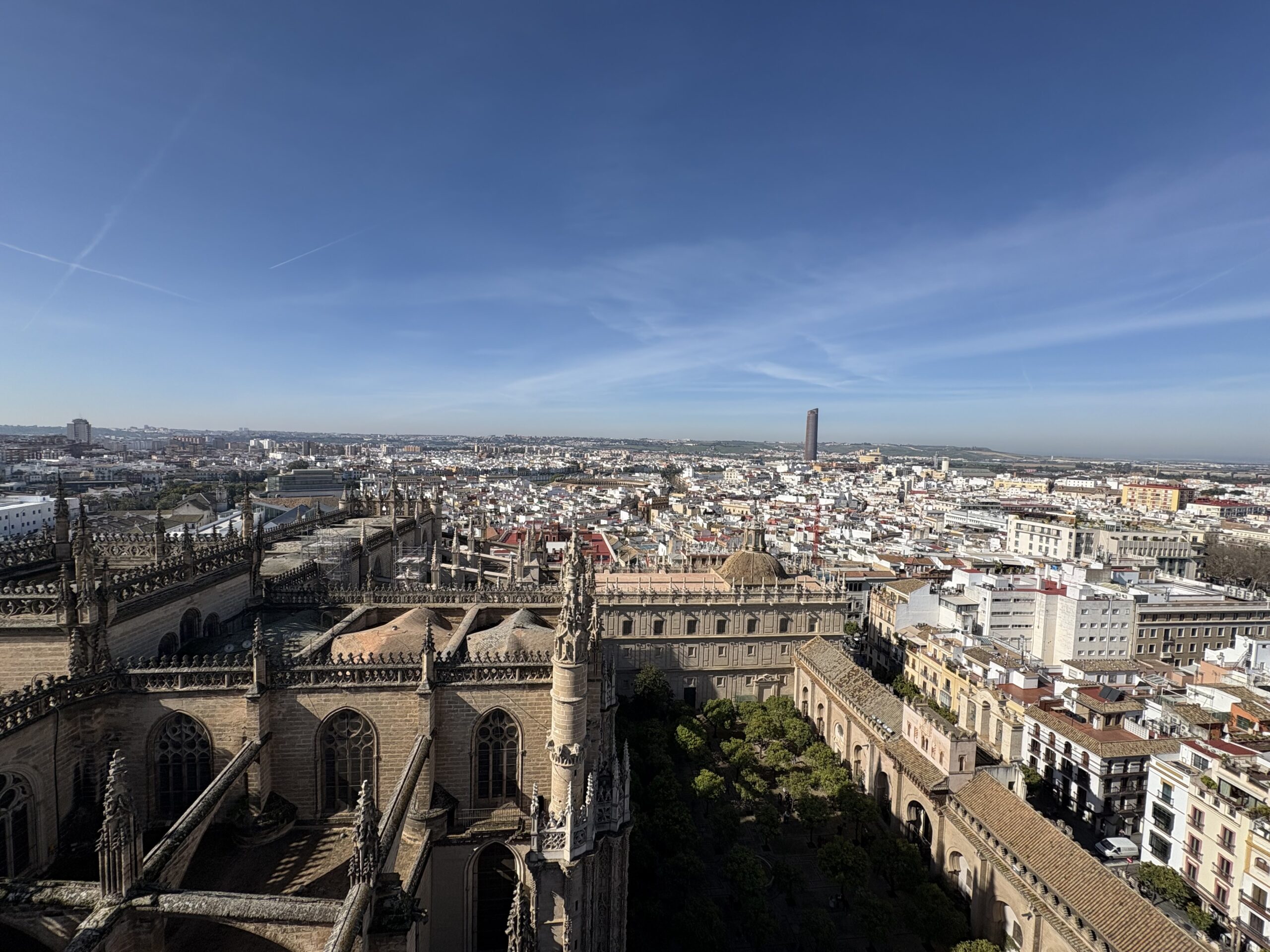A view of the city of Sevilla from the top of the Giralda of the Cathedral, the rest of the cathedral shown at the bottom and a cityscape above it, with a blue sky at the top