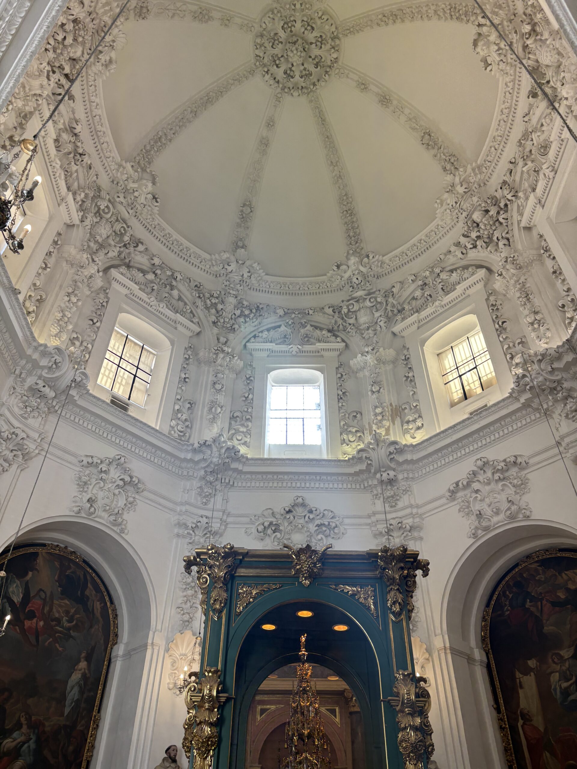A room in the Mosque-Cathedral of Córdoba, a large rounded white ceiling with intricate architecture, and a blue and gold rectangle frame at the bottom sided by an arch on either side