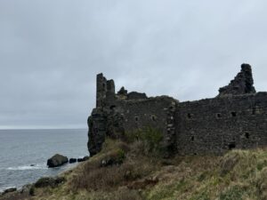 Castle in ruins on the edge of a cliff overlooking the ocean.