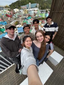 Busan Gamcheon Village which is made up of several colorful houses and buildings against a tall mountain range with students overlooking city city of a tall deck.