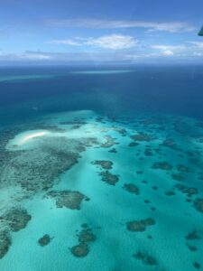 The Great Barrier Reef view from the scenic flight over the reef. Blue sky above and green ocean with coral formations.